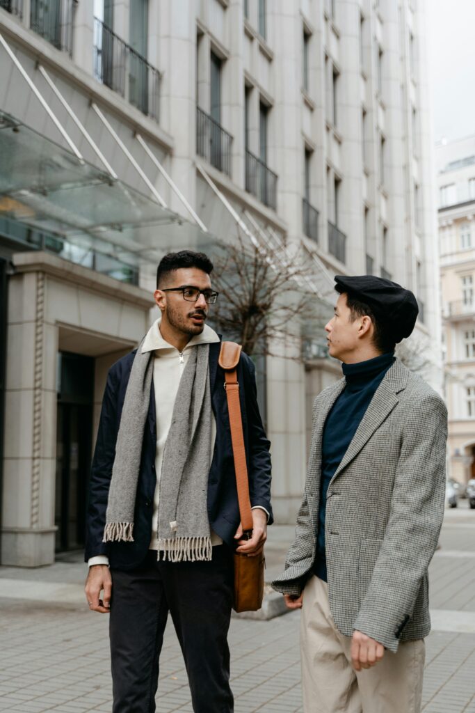 Two men in stylish blazers engaged in conversation outdoors in a city setting.